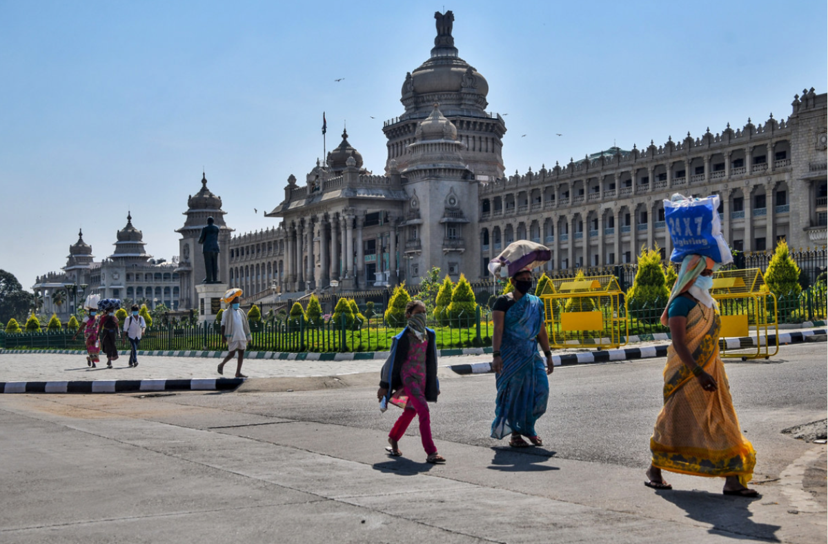 Image with people walking in a line, with bags on their head, wearing COVID-19 masks 